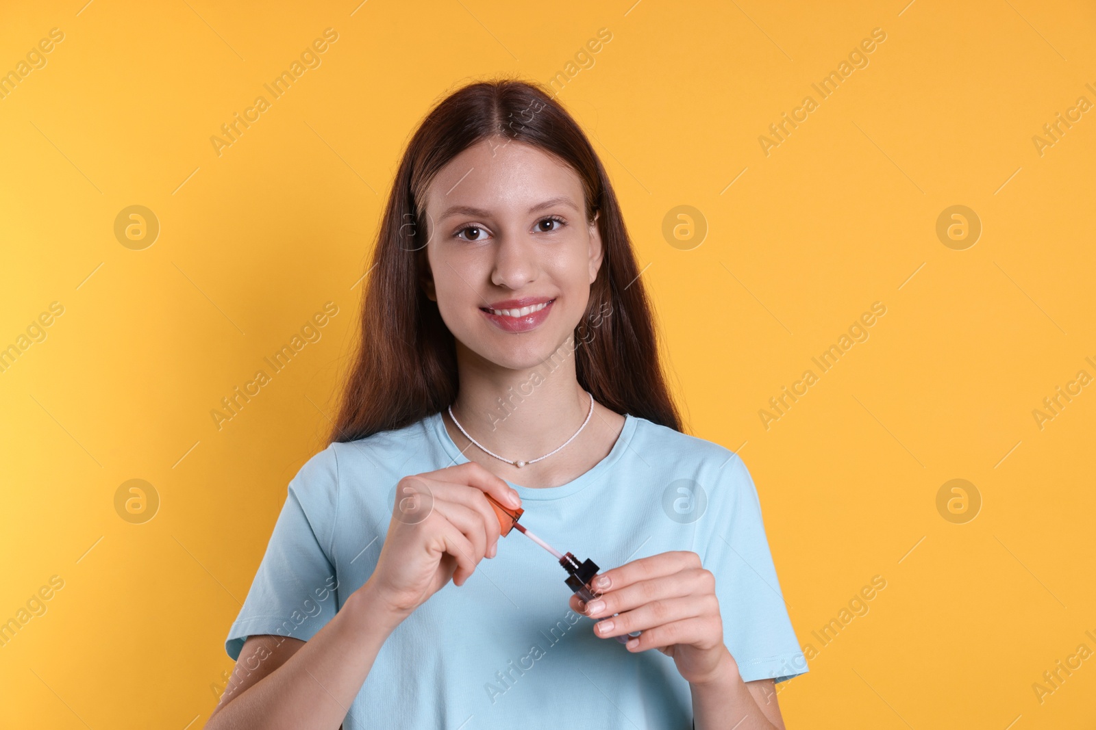 Photo of Smiling teenage girl with lip gloss on yellow background