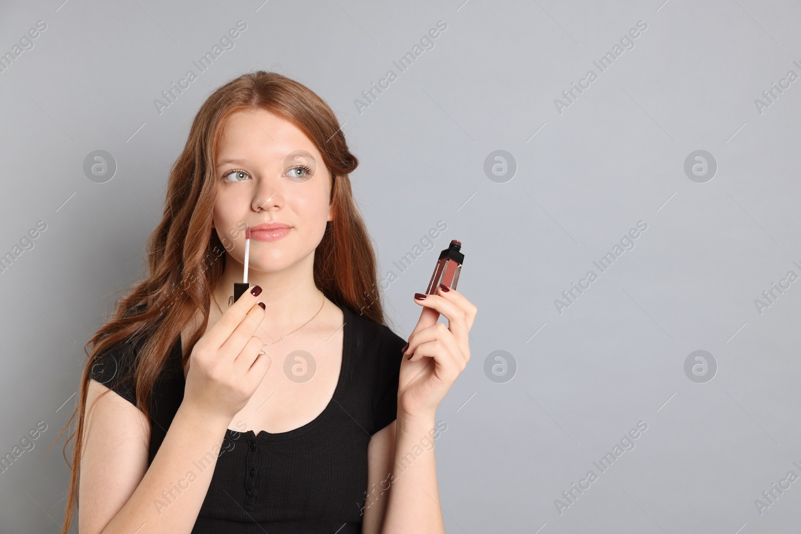 Photo of Teenage girl applying lip gloss on grey background. Space for text