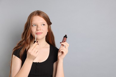 Photo of Teenage girl applying lip gloss on grey background. Space for text