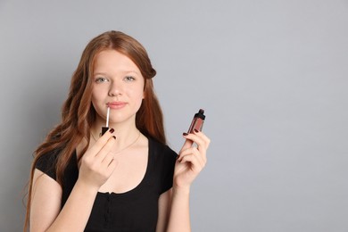 Photo of Teenage girl applying lip gloss on grey background. Space for text