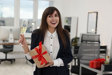 Photo of Happy woman with gift and glass of wine at office Christmas party