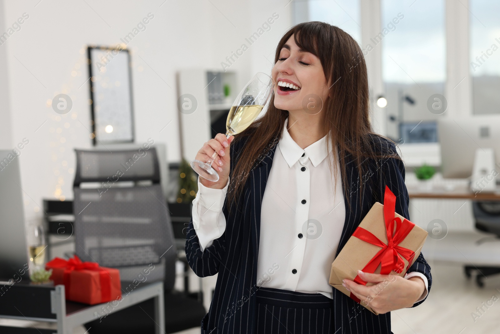 Photo of Happy woman with gift and glass of wine at office Christmas party