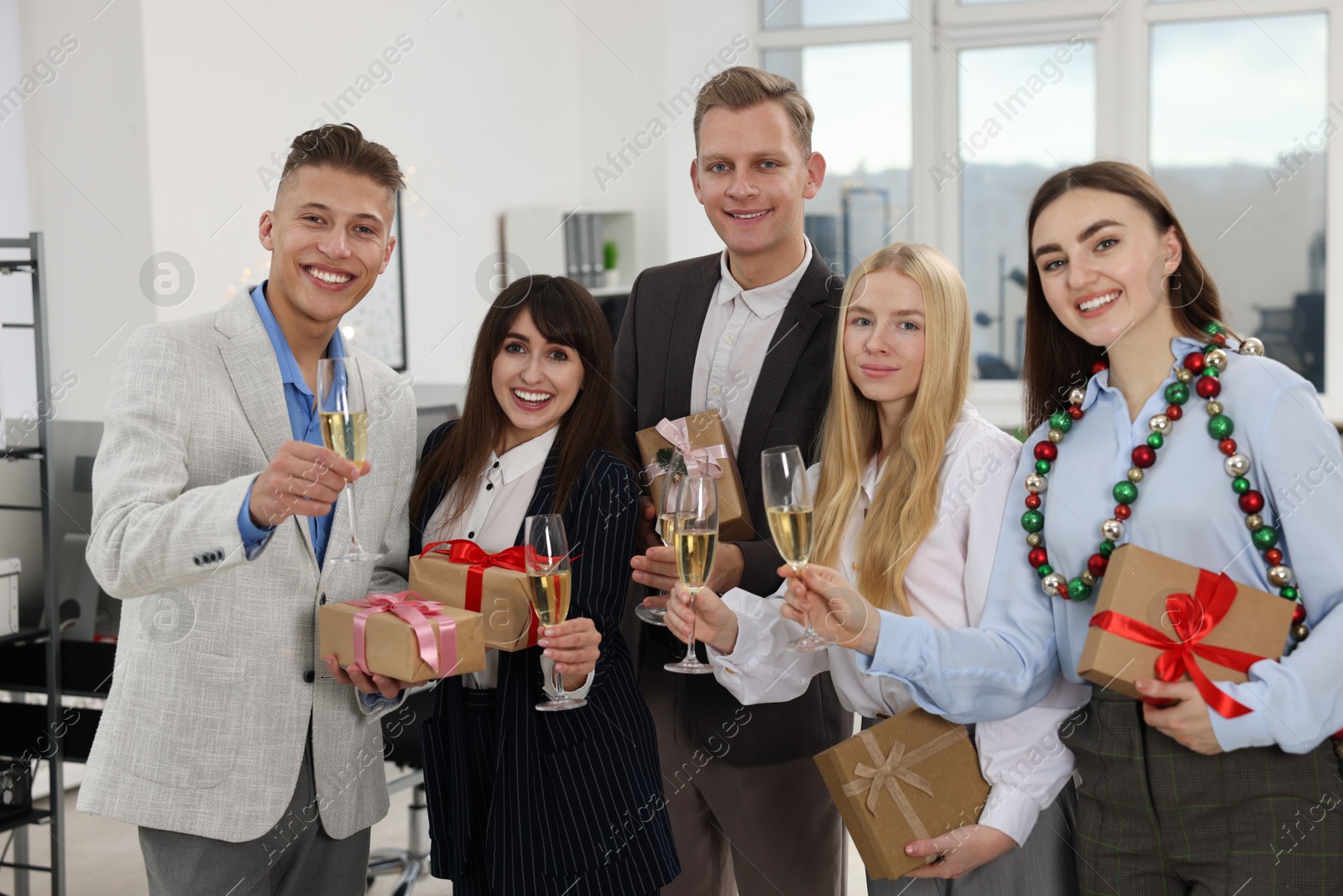 Photo of Cheerful coworkers with gifts and glasses of wine at Christmas party in office