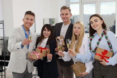 Photo of Cheerful coworkers with gifts and glasses of wine at Christmas party in office