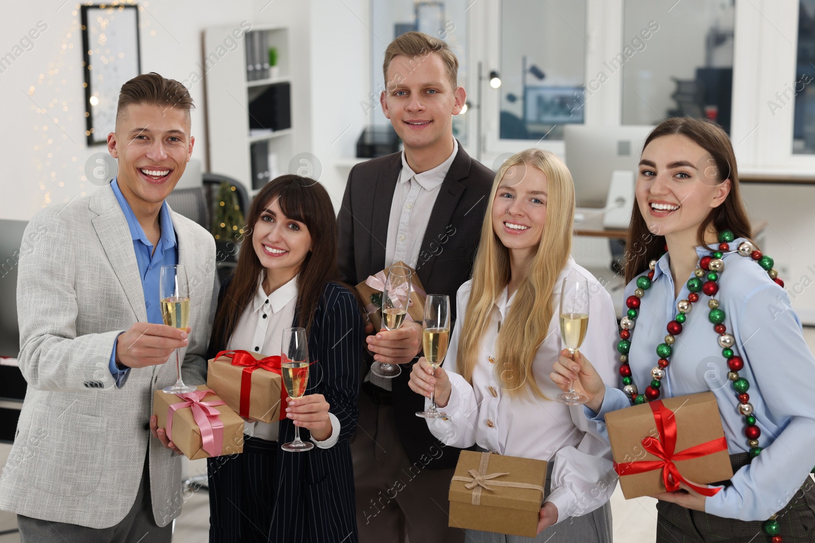 Photo of Cheerful coworkers with gifts and glasses of wine at Christmas party in office