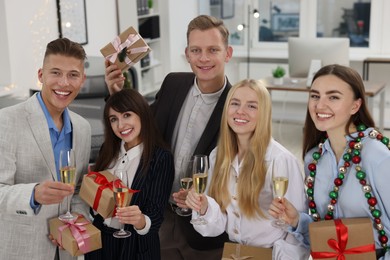 Photo of Cheerful coworkers with gifts and glasses of wine at Christmas party in office