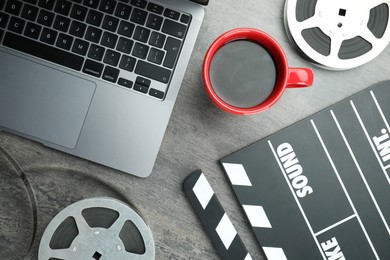 Photo of Flat lay composition with movie clapper, film reels and laptop on grey textured table