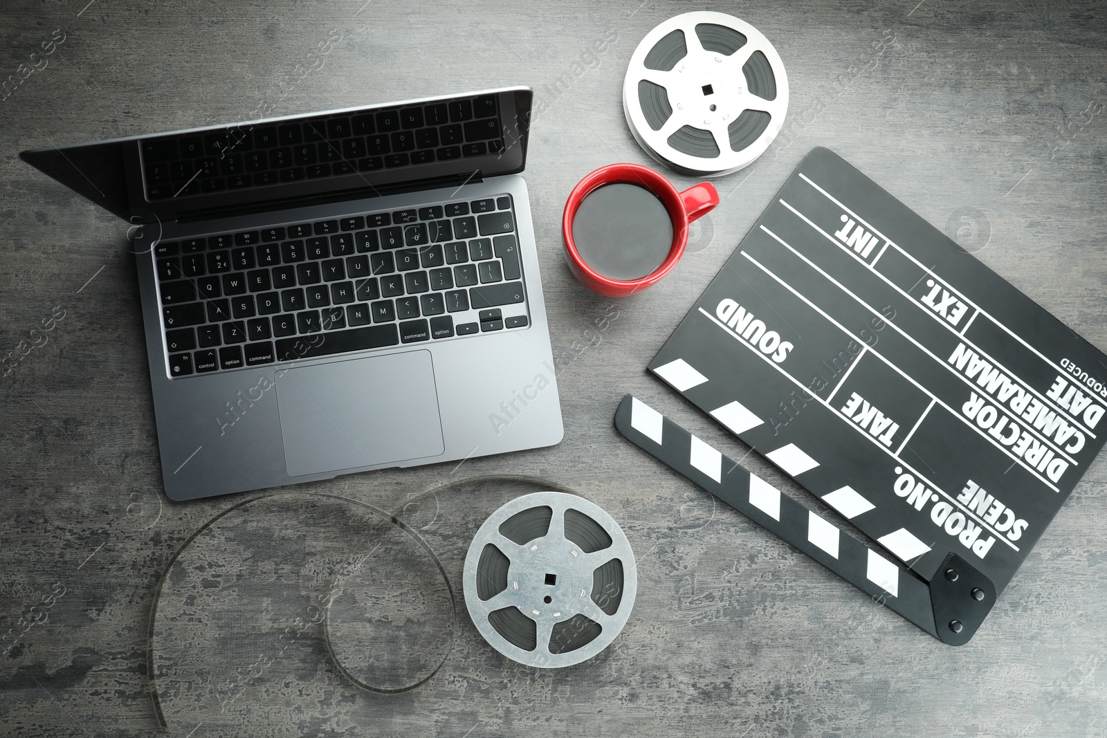 Photo of Flat lay composition with movie clapper, film reels and laptop on grey textured table