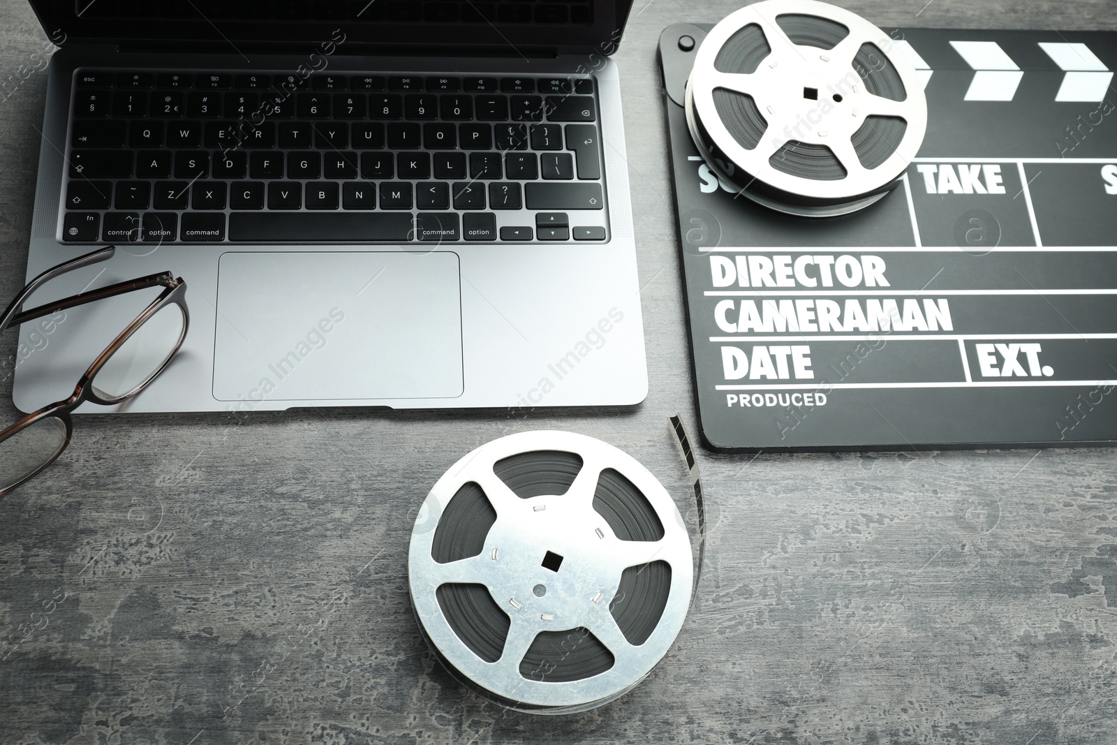 Photo of Movie clapper, film reels and laptop on grey textured table