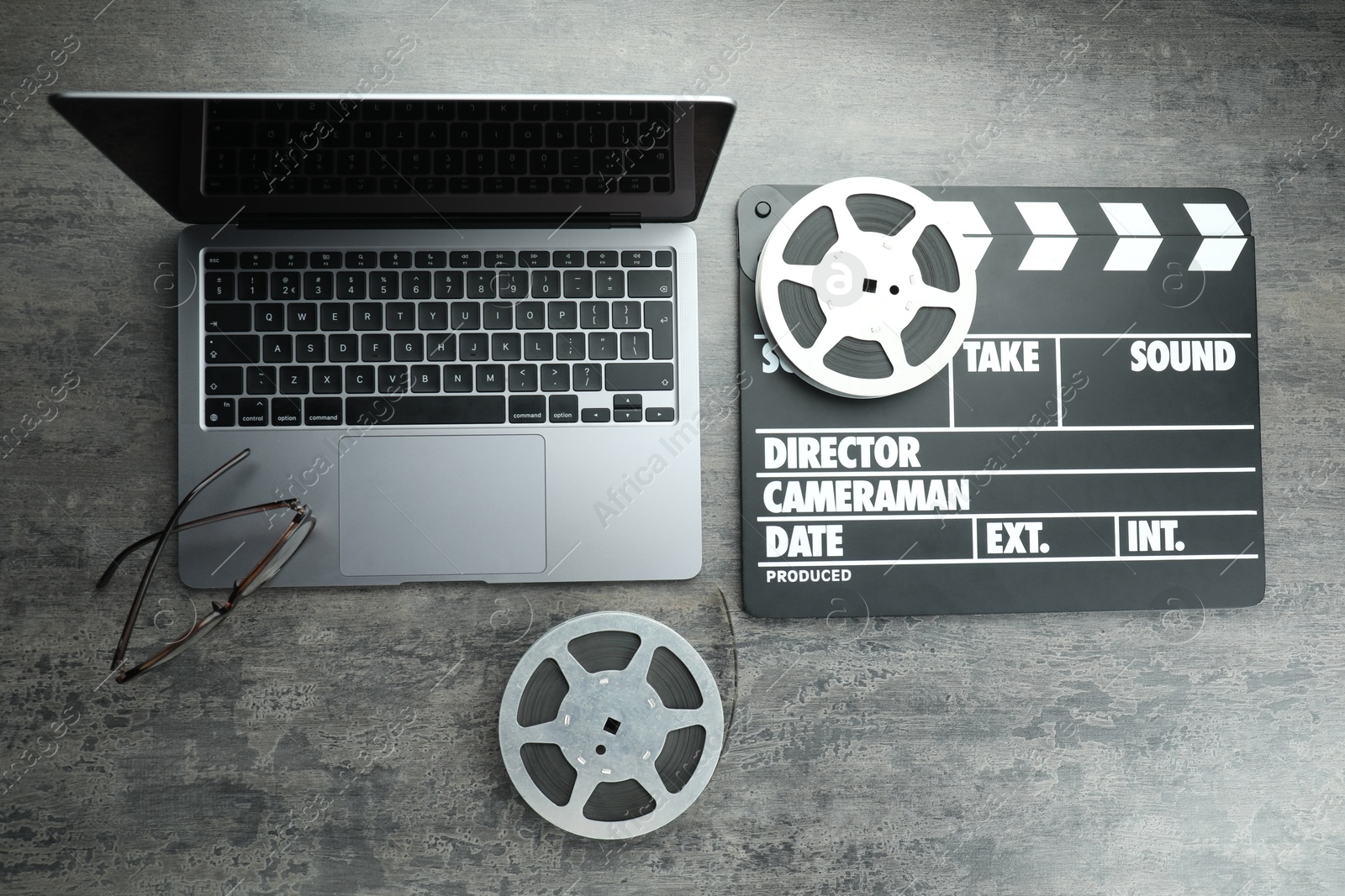 Photo of Movie clapper, film reels and laptop on grey textured table, flat lay