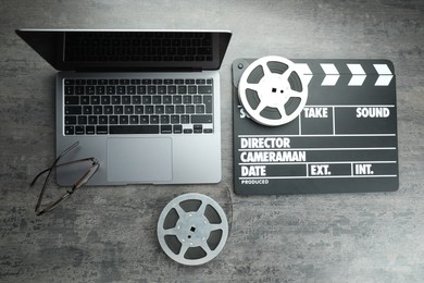 Photo of Movie clapper, film reels and laptop on grey textured table, flat lay