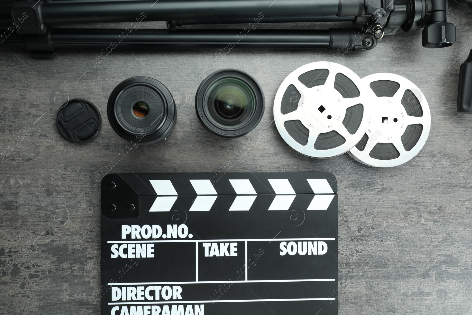 Photo of Flat lay composition with movie clapper, film reels and camera lens on grey textured table