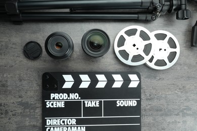 Photo of Flat lay composition with movie clapper, film reels and camera lens on grey textured table