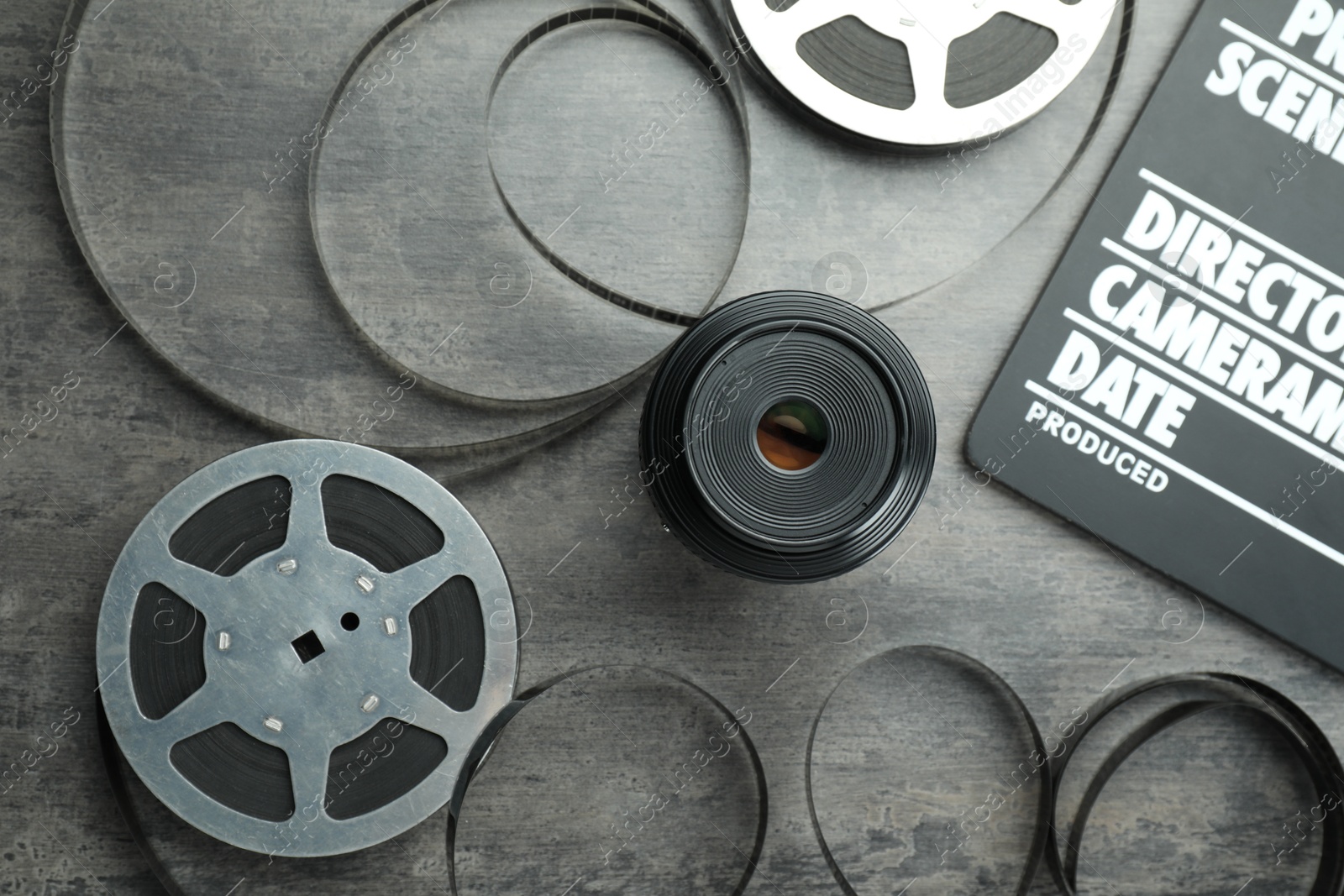 Photo of Flat lay composition with movie clapper, film reels and camera lens on grey textured table