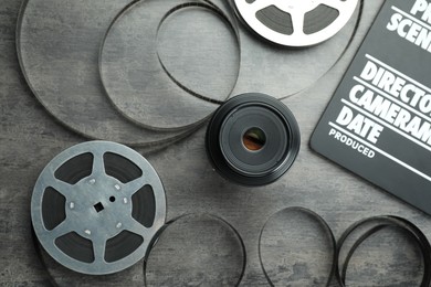 Photo of Flat lay composition with movie clapper, film reels and camera lens on grey textured table