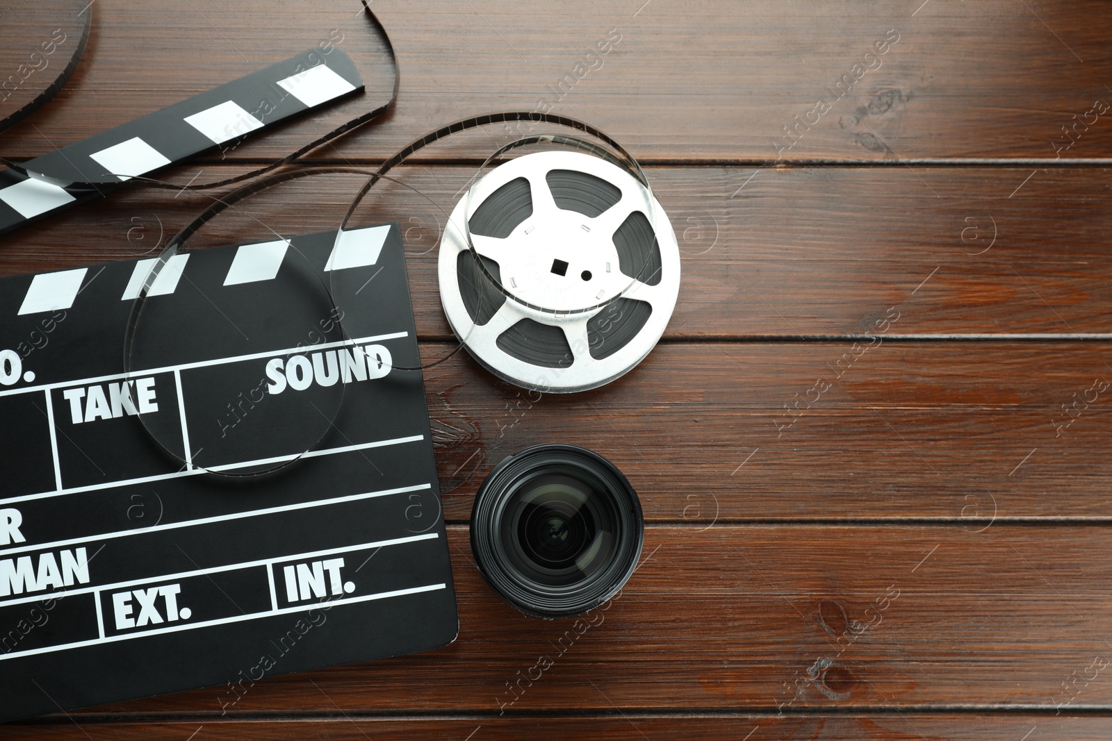 Photo of Flat lay composition with movie clapper, film reel and camera lens on wooden table. Space for text