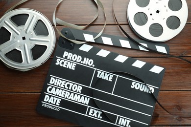 Photo of Movie clapper and film reels on wooden table, flat lay