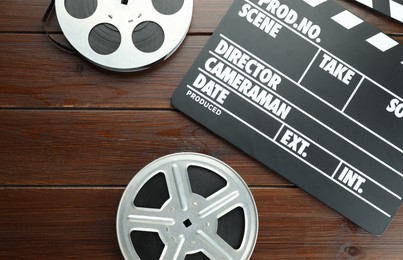 Photo of Movie clapper and film reels on wooden table, flat lay