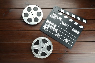 Photo of Movie clapper and film reels on wooden table, flat lay