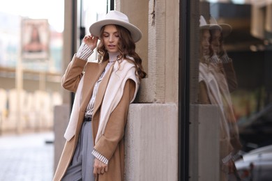 Charming young woman near shop on city street, space for text