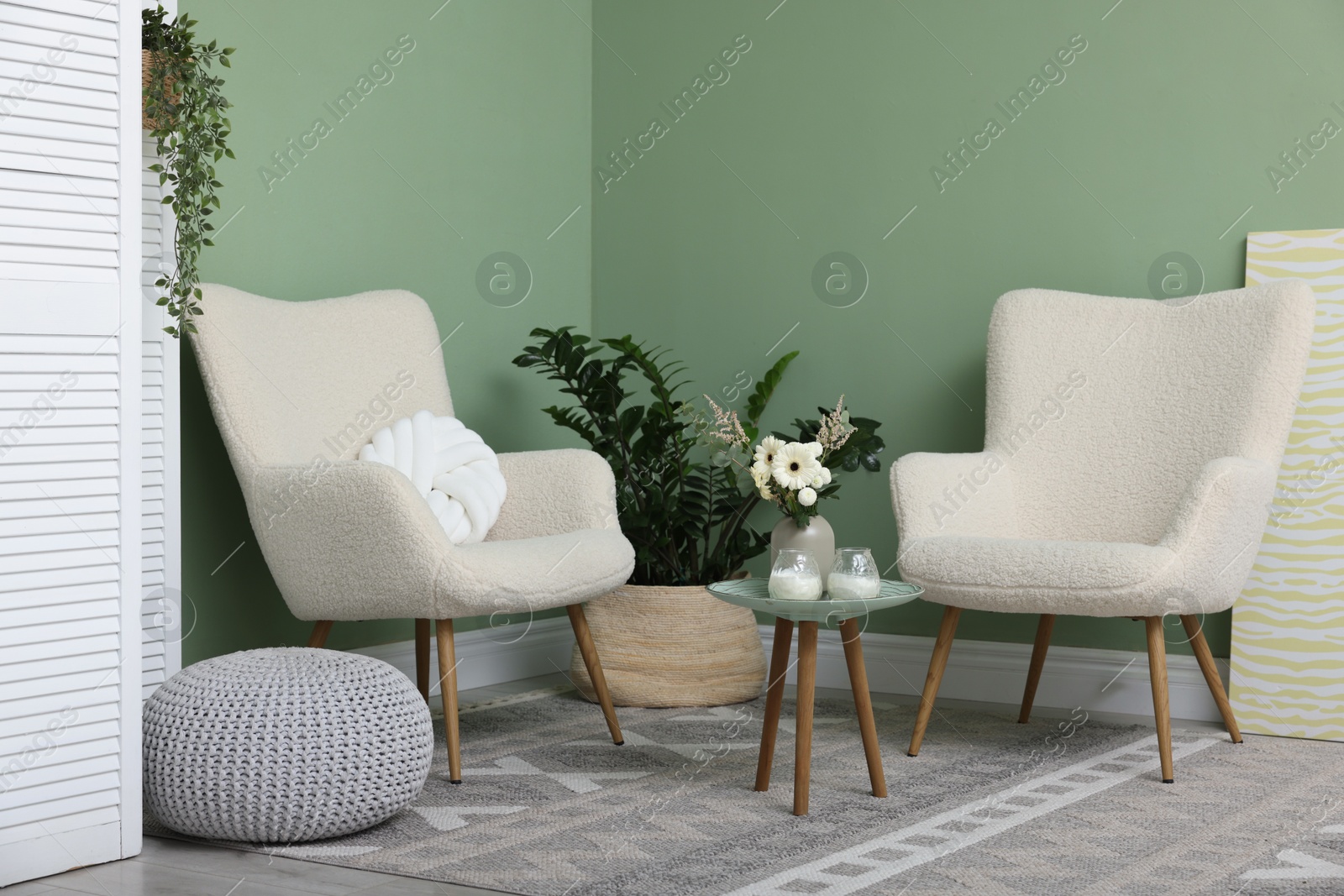 Photo of Soft armchairs, side table, folding screen and floral decor in room