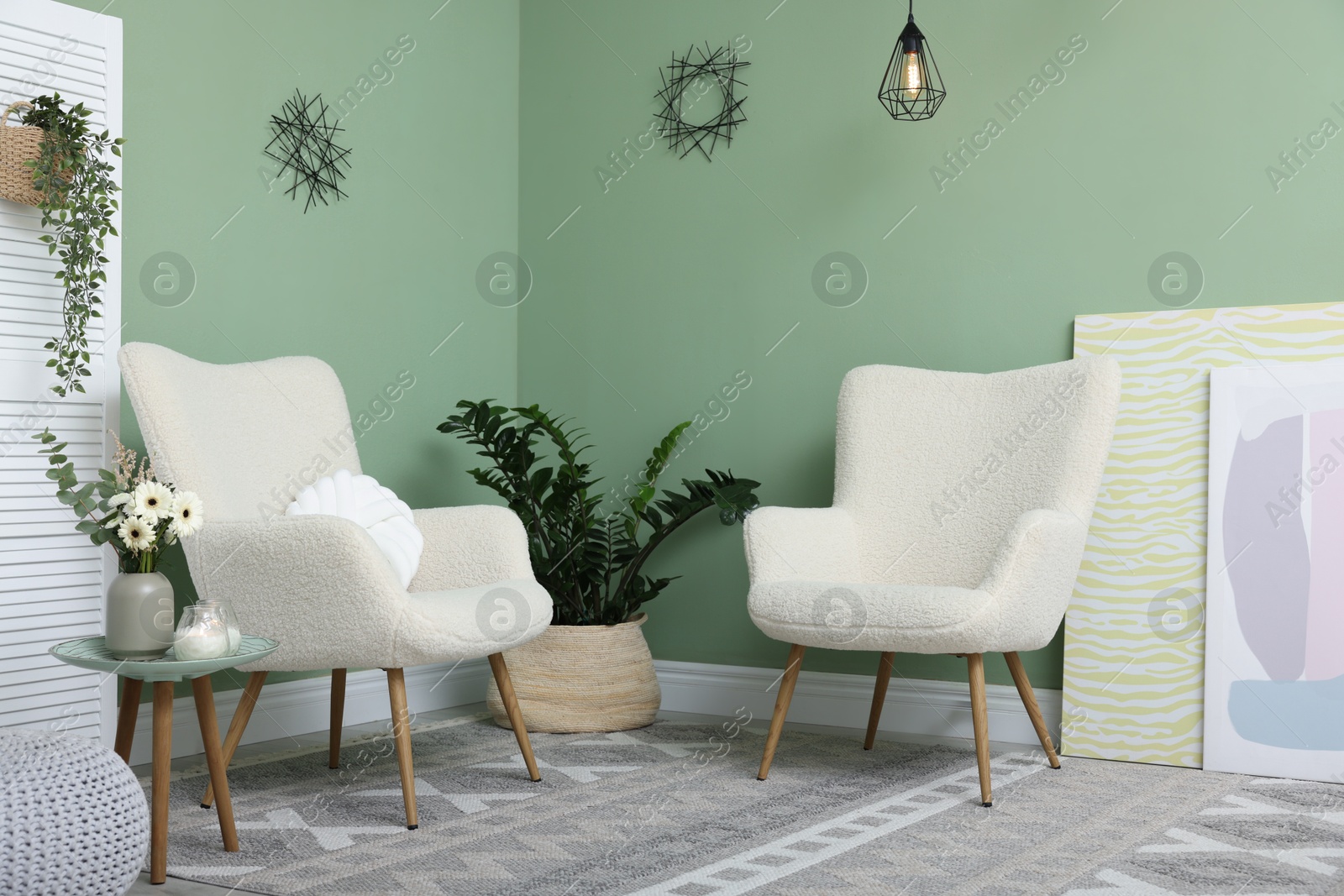 Photo of Soft armchairs, side table, folding screen and floral decor in room