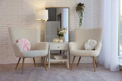 Photo of Soft armchairs, side table, mirror and floral decor in room