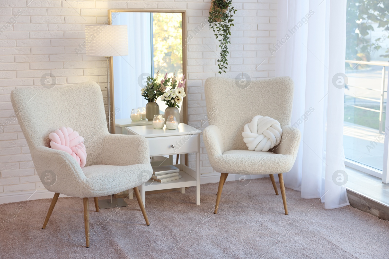 Photo of Soft armchairs, side table, mirror and floral decor in room