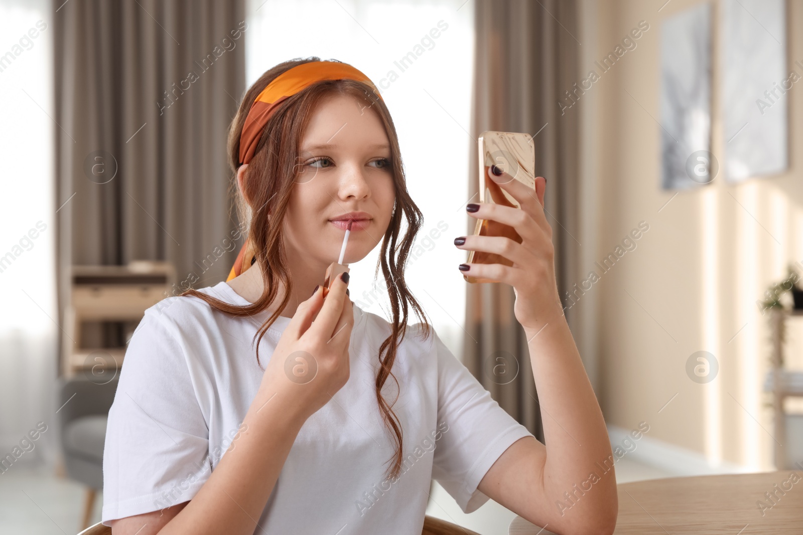 Photo of Teenage girl applying lip gloss at home