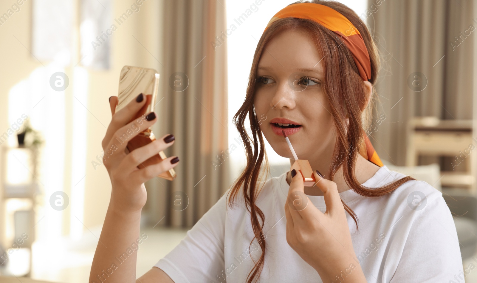 Photo of Teenage girl applying lip gloss at home