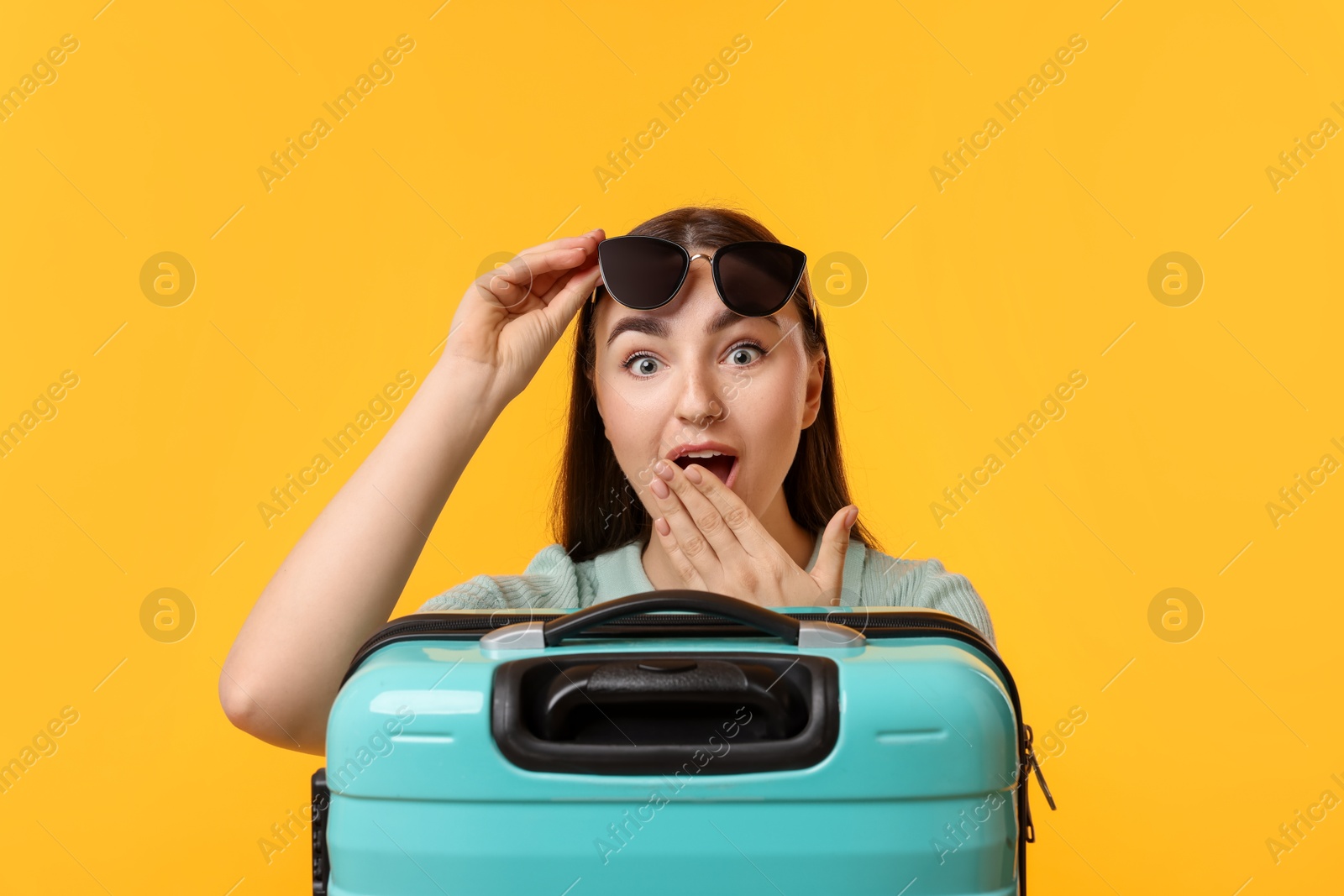 Photo of Emotional woman with suitcase wearing sunglasses on orange background