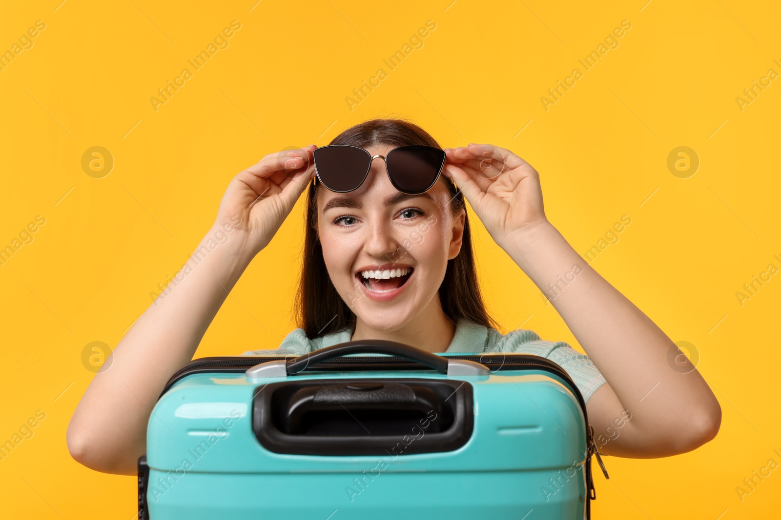 Photo of Woman with suitcase wearing sunglasses on orange background