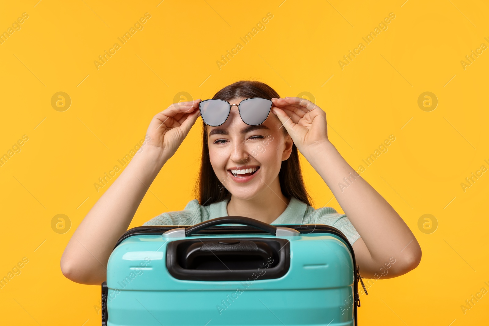 Photo of Woman with suitcase wearing sunglasses on orange background