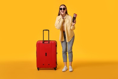 Photo of Woman with tickets, passport and suitcase on orange background