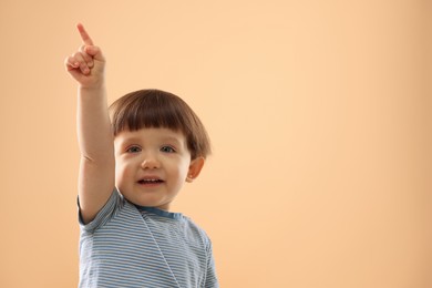 Photo of Portrait of cute little boy pointing upwards on beige background. Space for text