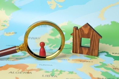 Photo of Wooden house model, magnifying glass and red human figure on world map. Accommodation search