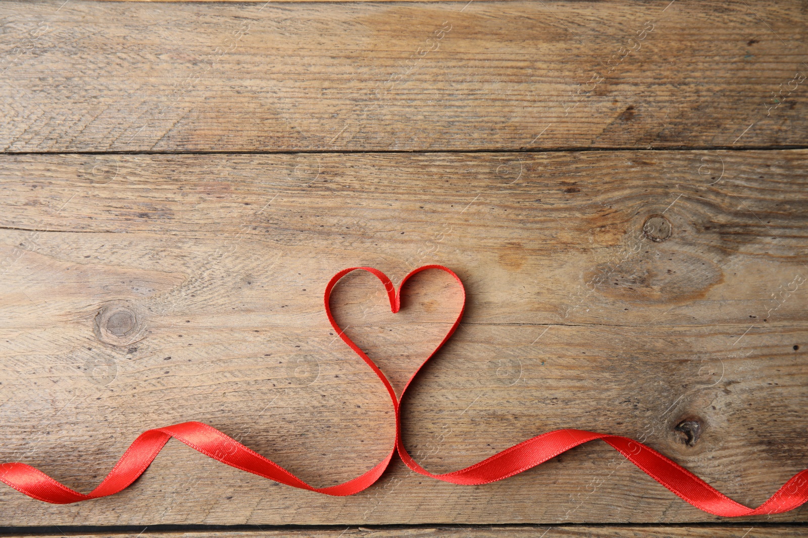 Photo of Heart made of red ribbon on wooden background, top view with space for text. Valentine's day celebration