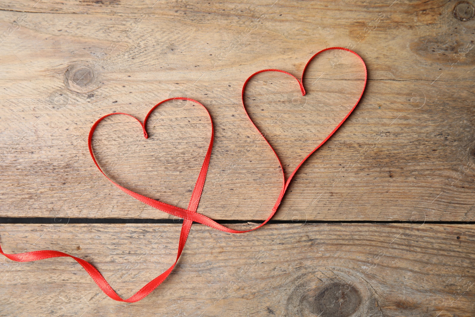 Photo of Hearts made of red ribbon on wooden background, top view. Valentine's day celebration