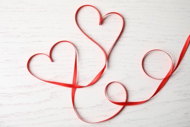 Photo of Hearts made of red ribbon on white wooden background, top view. Valentine's day celebration