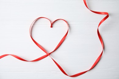 Photo of Heart made of red ribbon on white wooden background, top view. Valentine's day celebration