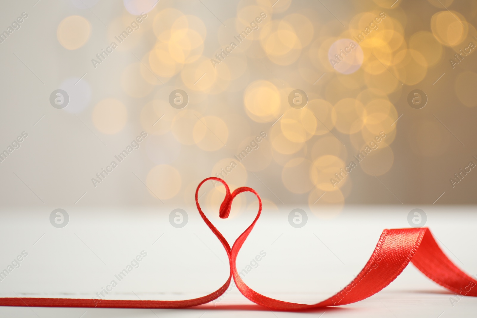 Photo of Heart made of red ribbon on table against blurred festive lights, space for text. Valentine's day celebration