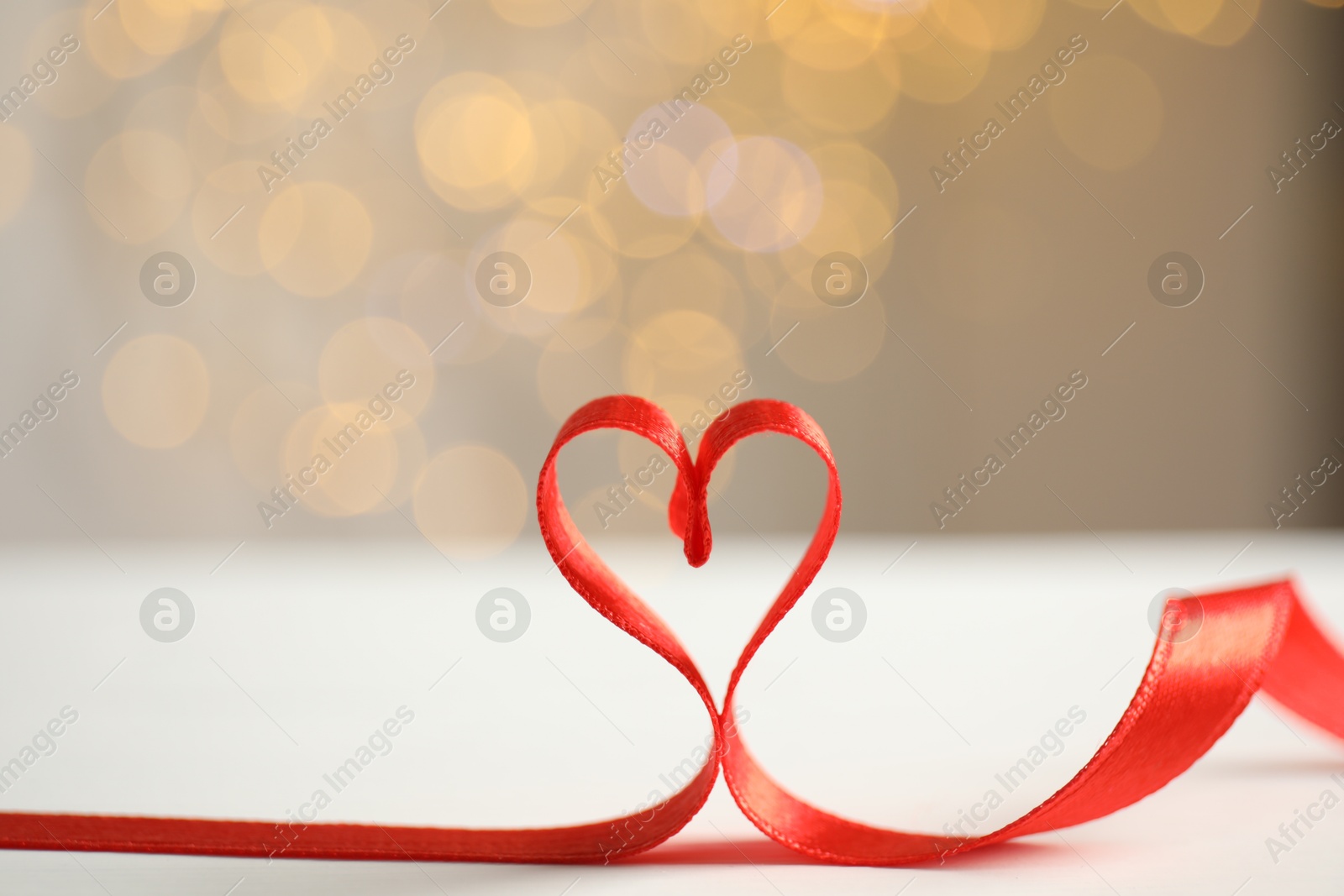 Photo of Heart made of red ribbon on table against blurred festive lights. Valentine's day celebration