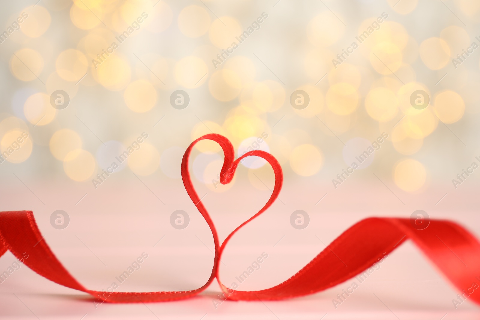 Photo of Heart made of red ribbon on table against blurred lights. St. Valentine's day card