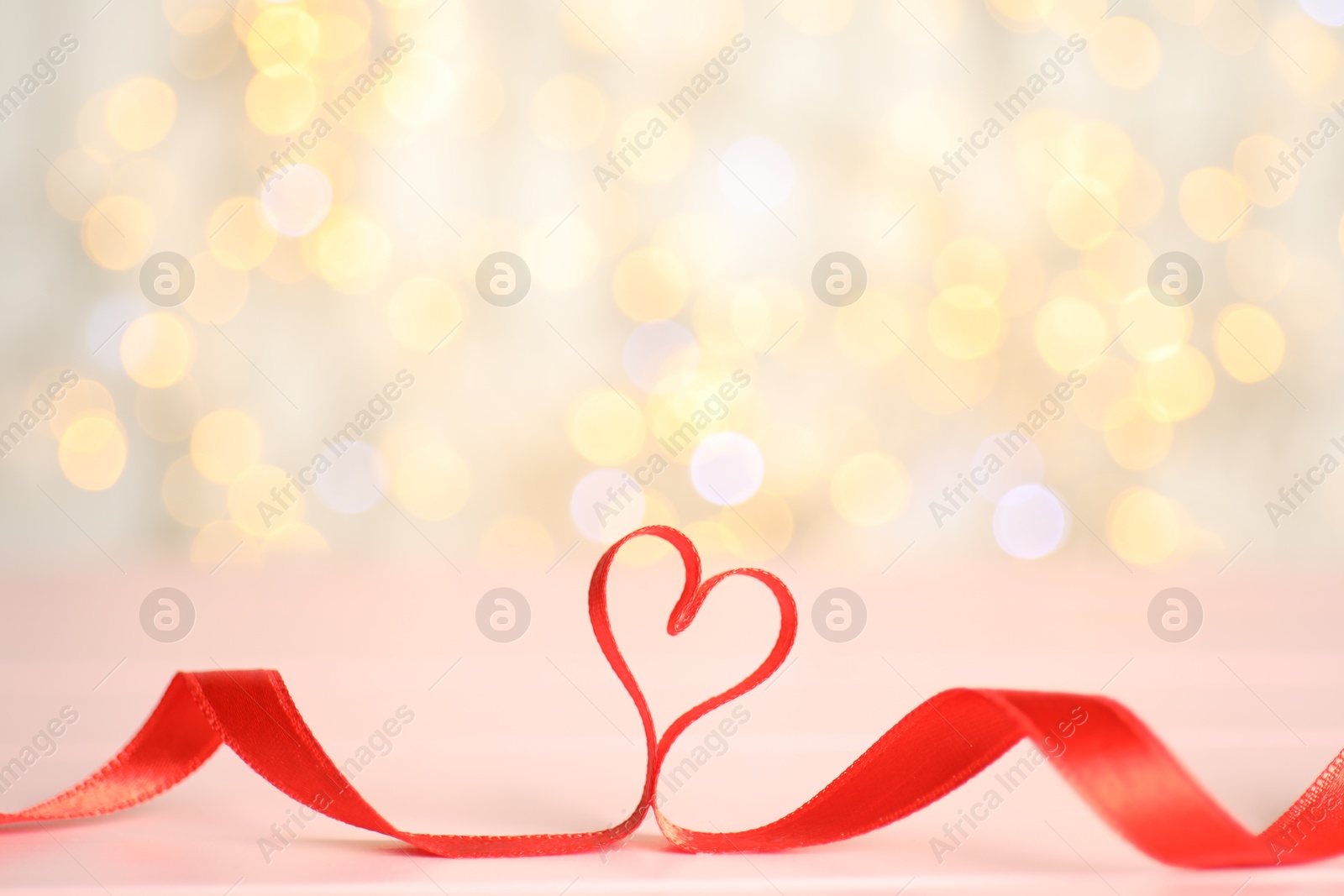 Photo of Heart made of red ribbon on table against blurred lights, space for text. St. Valentine's day card