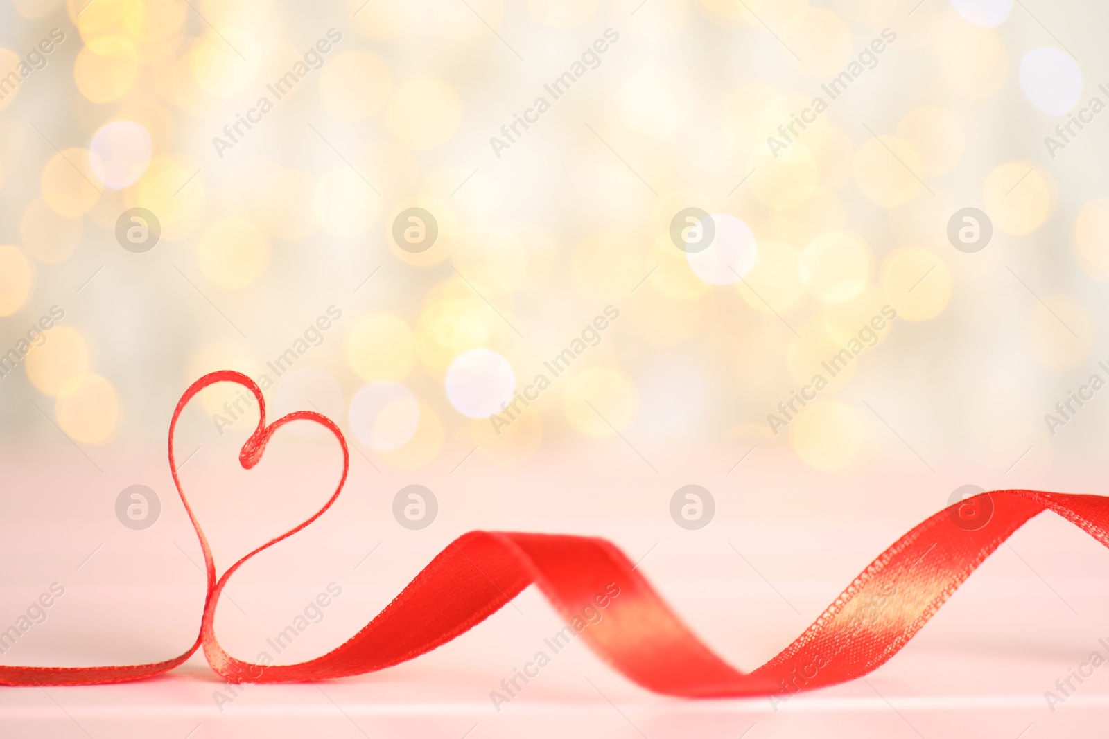 Photo of Heart made of red ribbon on table against blurred lights, space for text. St. Valentine's day card