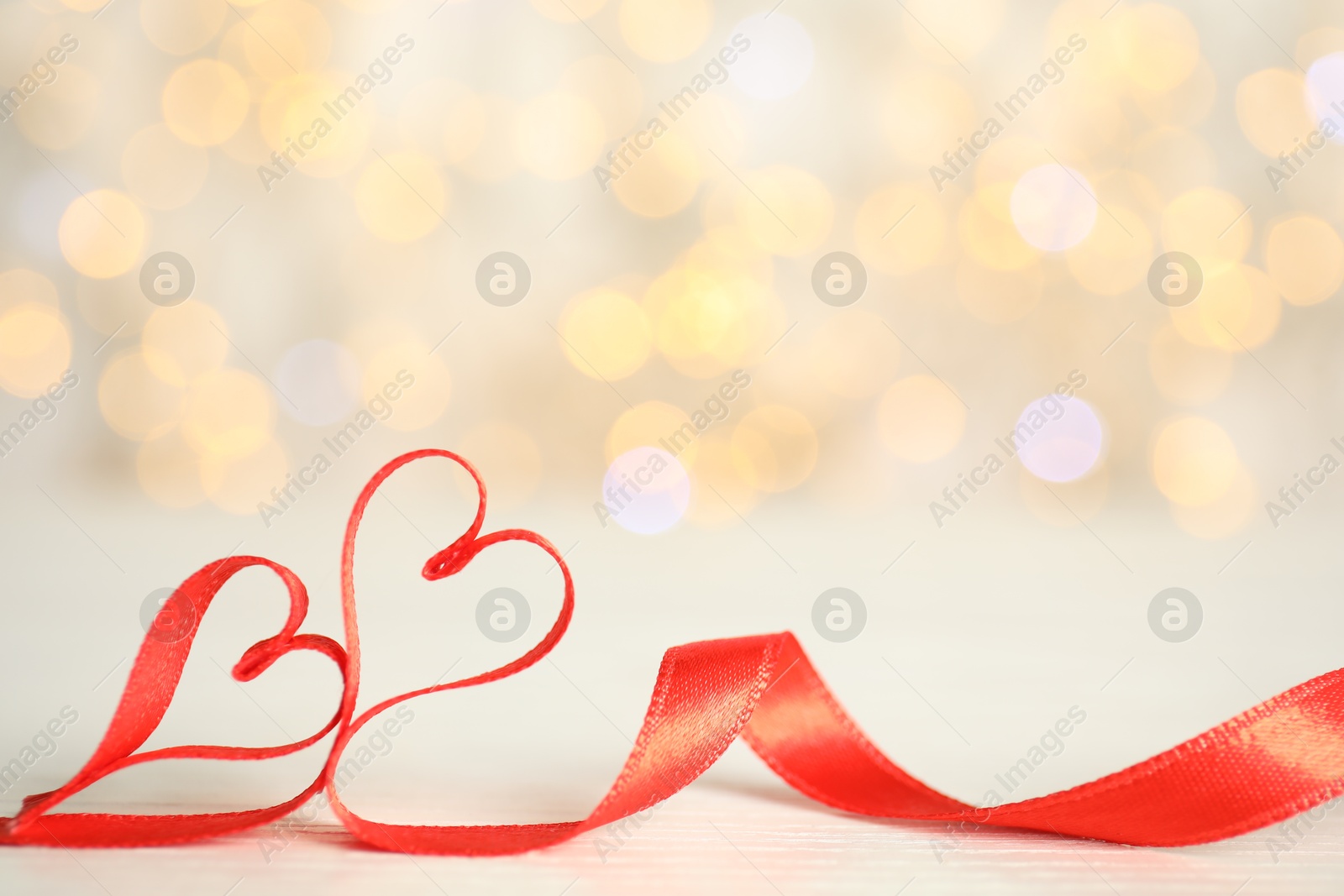 Photo of Two hearts made of red ribbon on table against blurred lights, space for text. St. Valentine's day card