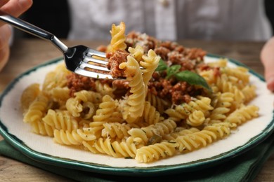 Photo of Woman eating delicious pasta with minced meat and basil at table, closeup