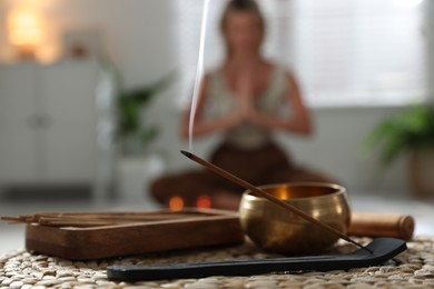 Photo of Incense stick smoldering in holder and tibetan singing bowl indoors, selective focus