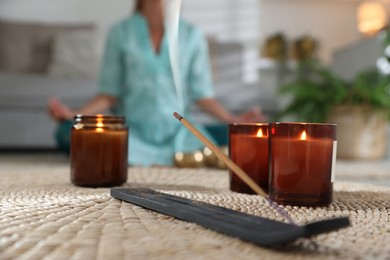 Photo of Incense stick smoldering in holder and burning candles on wicker mat indoors, selective focus