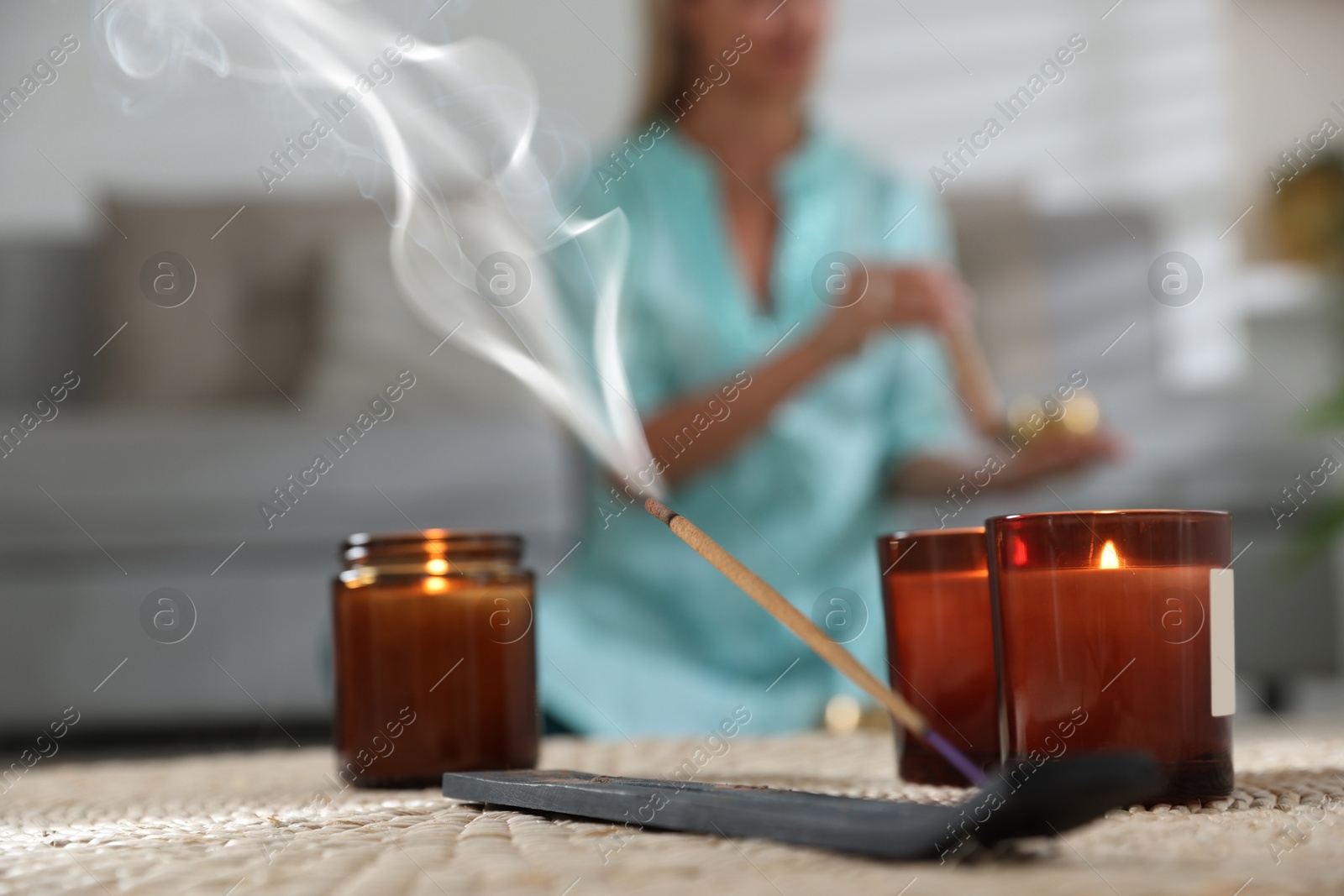 Photo of Incense stick smoldering in holder and burning candles on wicker mat indoors, selective focus